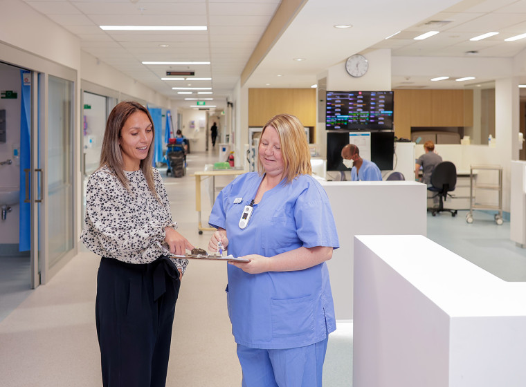 Two women standing in the hallway of a hospital reviewing patient notes